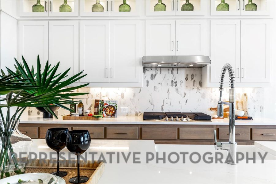 Kitchen featuring under cabinet range hood, backsplash, white cabinets, and light countertops Kitchen featuring under cabinet range hood, backsplash, white cabinets, and light countertops