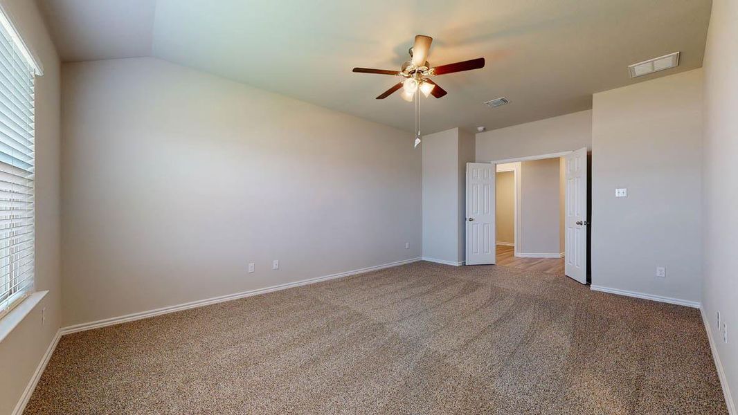 Spacious room featuring vaulted ceilings, neutral carpet flooring, a ceiling fan with integrated lighting, and a large window with blinds