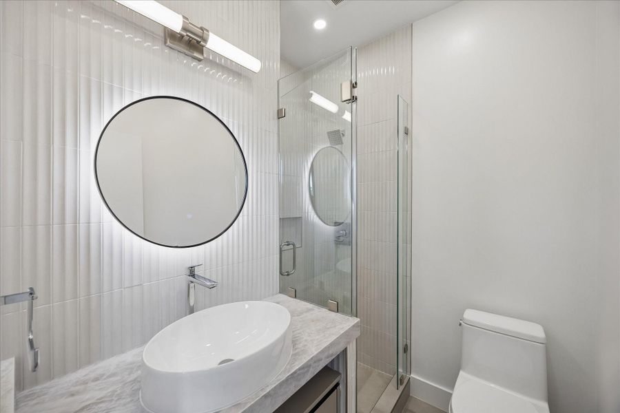 Modern bathroom with glass-enclosed shower, stylish round mirror with backlighting, and elegant vessel sink on a marble countertop. Modern bathroom with glass-enclosed shower, stylish round mirror with backlighting, and elegant vessel sink on a marble countertop.