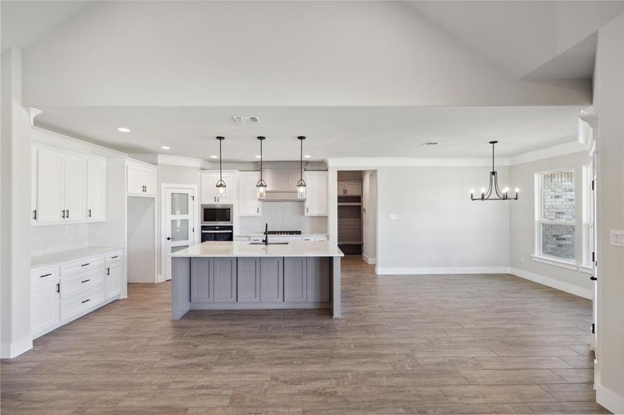 Kitchen featuring pendant lighting, a kitchen island with sink, sink, stainless steel microwave, and light hardwood / wood-style flooring