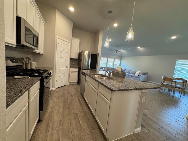 Spacious kitchen featuring granite countertops, stainless steel appliances, wood-finish flooring, white cabinetry, and an island with a double sink Spacious kitchen featuring granite countertops, stainless steel appliances, wood-finish flooring, white cabinetry, and an island with a double sink