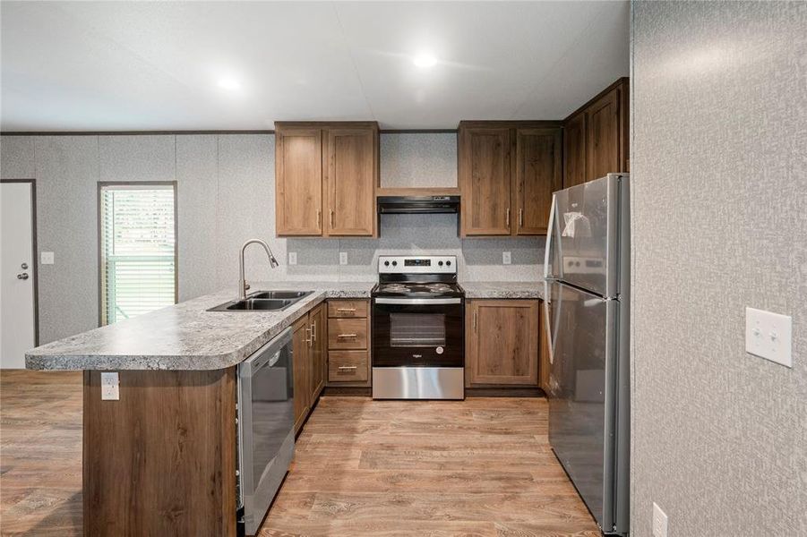 Kitchen with appliances with stainless steel finishes, ventilation hood, light wood-type flooring, a peninsula, and light countertops