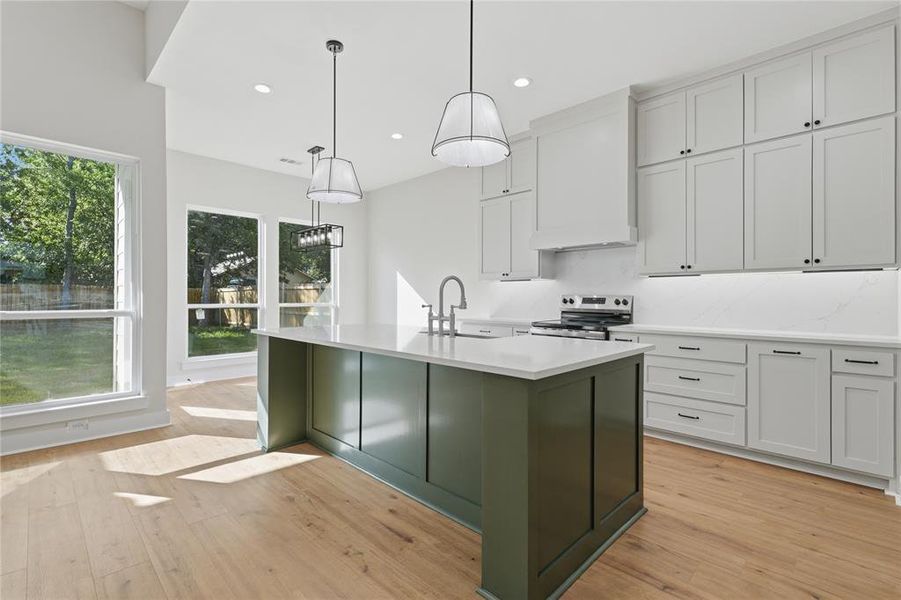 Kitchen featuring a large central island with a deep green finish, light wood-finish flooring, white perimeter cabinetry, stainless steel range, and multiple windows Kitchen featuring a large central island with a deep green finish, light wood-finish flooring, white perimeter cabinetry, stainless steel range, and multiple windows