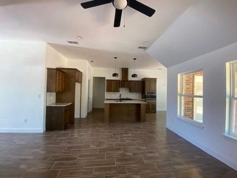 Kitchen featuring decorative backsplash, a ceiling fan, an island with sink, baseboards, and open floor plan
