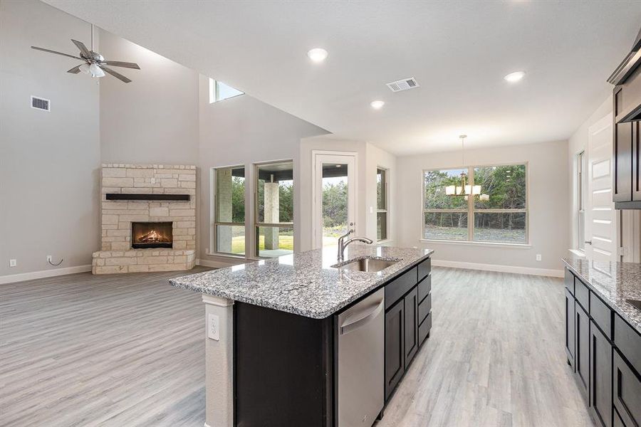 Kitchen featuring sink, stainless steel dishwasher, an island with sink, decorative light fixtures, and a fireplace