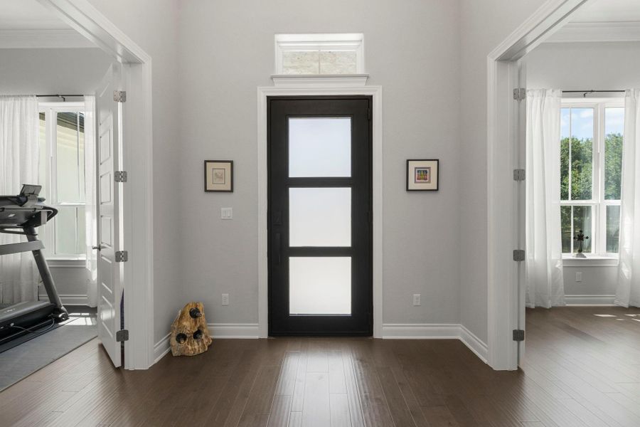 Enter through a distinctive front door with privacy glass, flanked by bright rooms and rich wood floors.