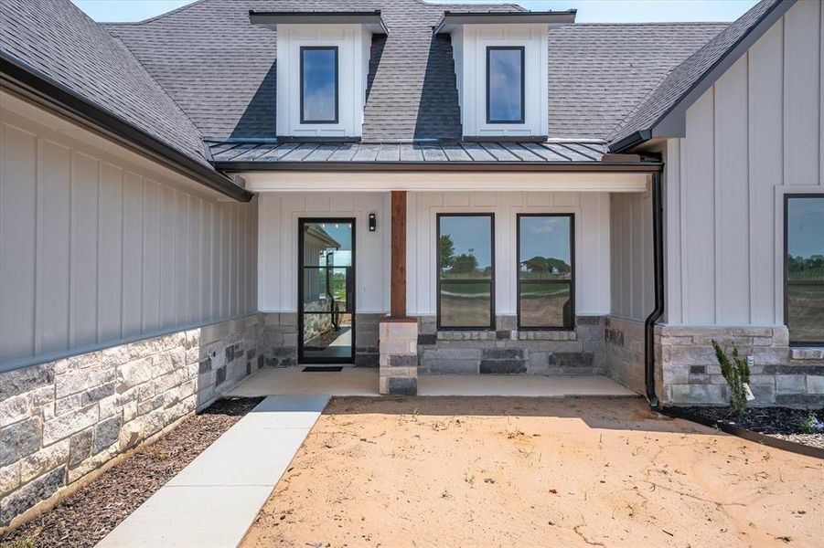 Property entrance featuring a standing seam roof, a shingled roof, a metal roof, and stone siding