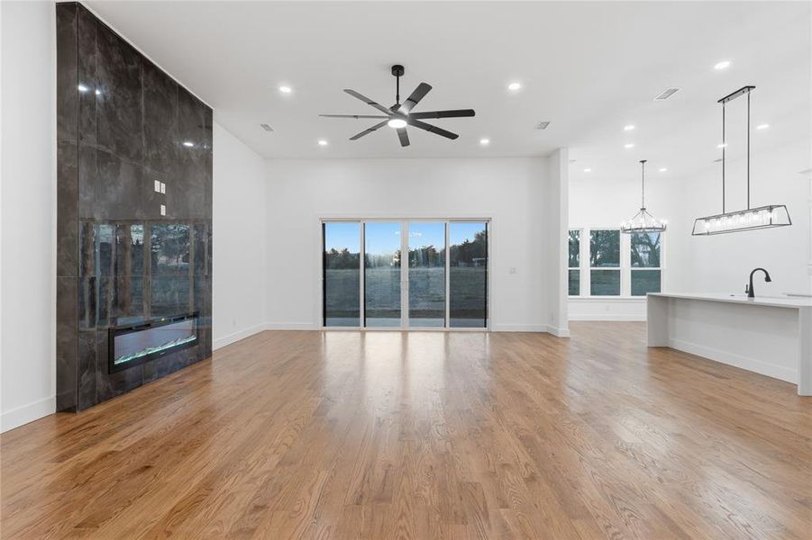 Unfurnished living room with a ceiling fan, light wood finished floors, a tile fireplace, a high ceiling, and hanging lights