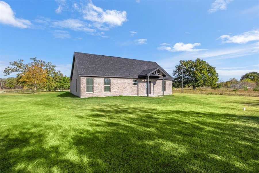 Back of house featuring a lawn, a shingled roof, and brick siding