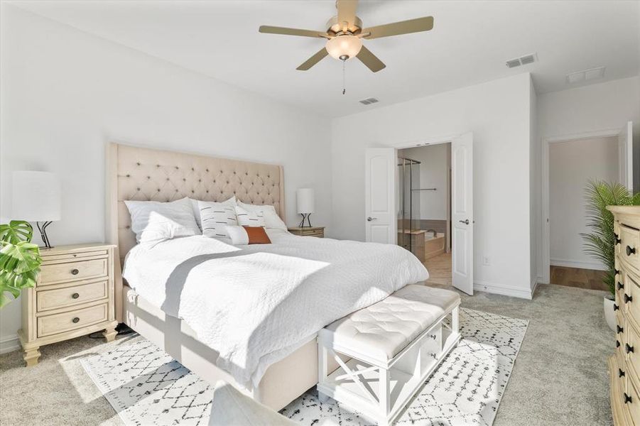Spacious bedroom featuring light-toned carpeting, a ceiling fan with integrated lighting, and white double doors leading to an adjoining bathroom