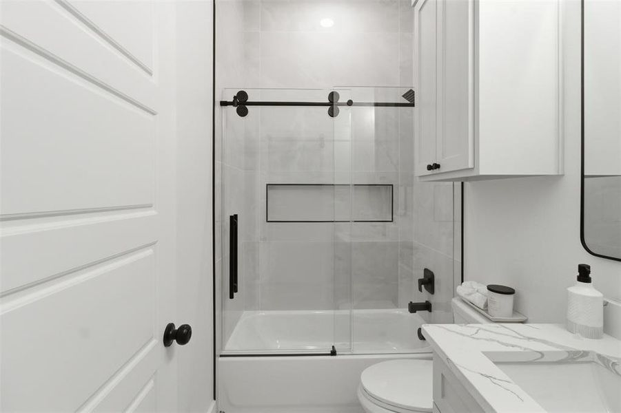 Modern bathroom featuring a white panel door, sliding glass shower enclosure with matte black hardware, white subway tile shower surround with recessed niche, and a white vanity with integrated sink and stone-finish countertop