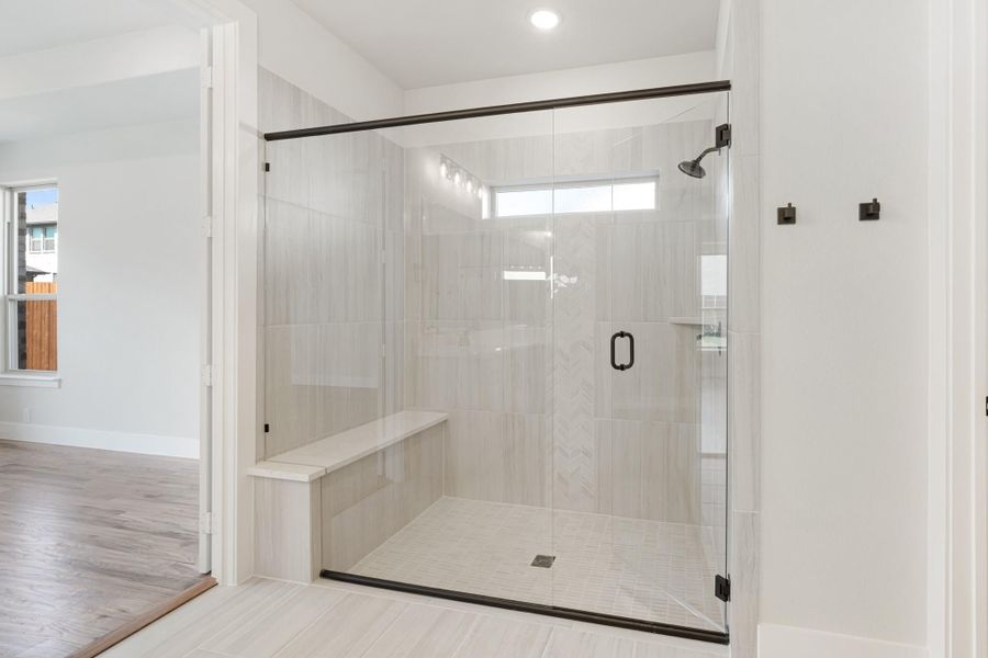 Walk-in shower with glass door, light tile walls, built-in bench, and dark metal hardware