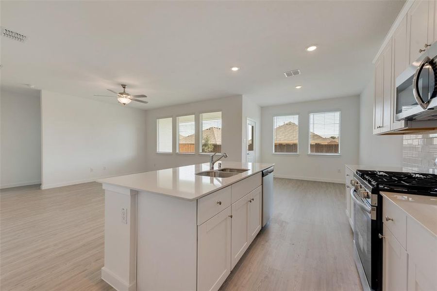 Kitchen featuring sink, tasteful backsplash, a center island with sink, white cabinetry, and appliances with stainless steel finishes