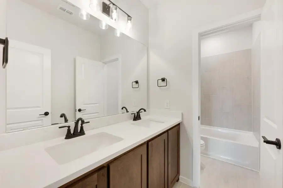 Bathroom with double sink vanity, wood cabinets, white countertop, and tiled tub-shower combo