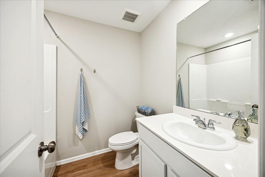 This bathroom features a clean, modern design with a white vanity, spacious mirror, and vinyl-style flooring. It includes a bathtub with a shower, and neutral tones create a bright, inviting space.