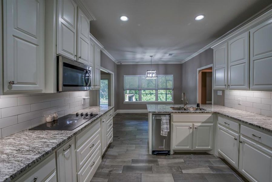 Kitchen with white cabinetry, black electric stovetop, kitchen peninsula, and double sink also please note the compactor to the left