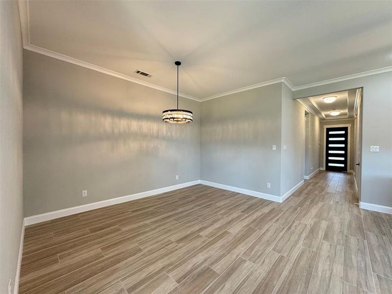 Spacious room featuring wood-finish tile flooring, crown molding, and a contemporary chandelier
