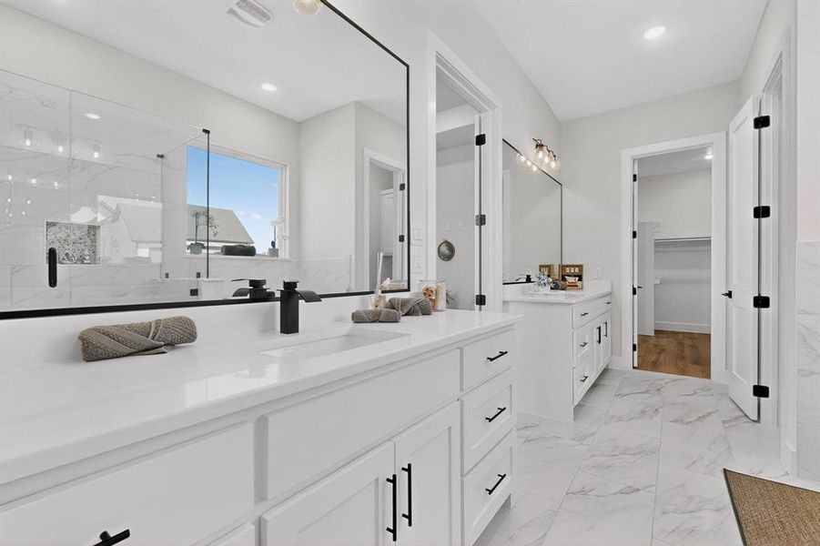 Full bath with two vanities, light marble finish flooring, a marble finish shower, a walk in closet, and recessed lighting