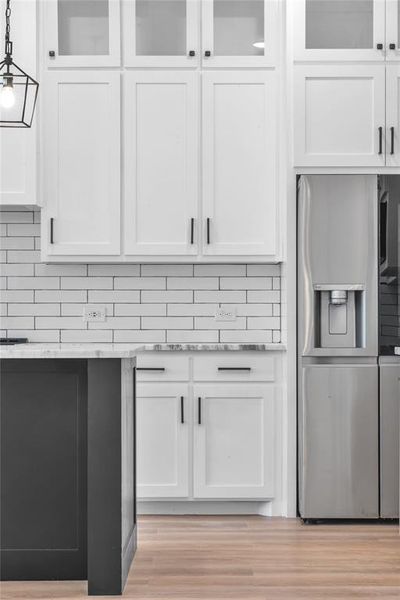 Room details with white cabinets, decorative backsplash, stainless steel fridge, light wood-type flooring, and decorative light fixtures