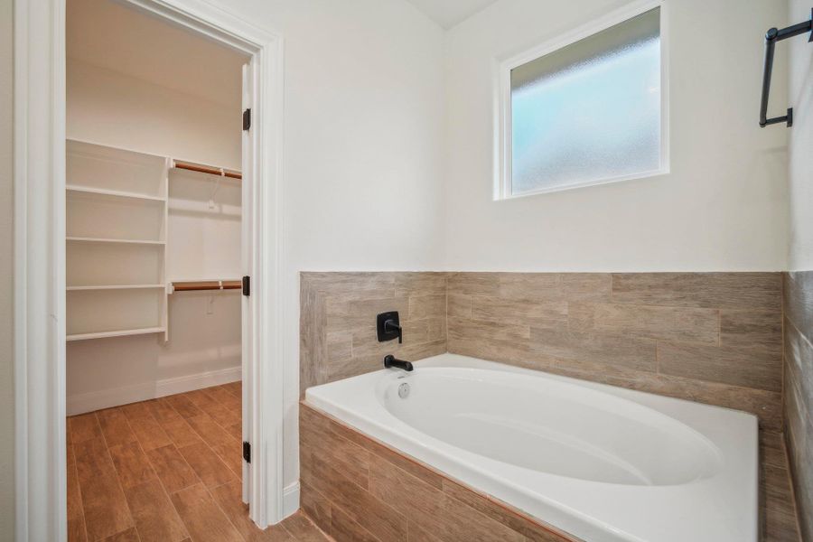 Bathroom with a walk in closet, wood finished floors, baseboards, and a bath