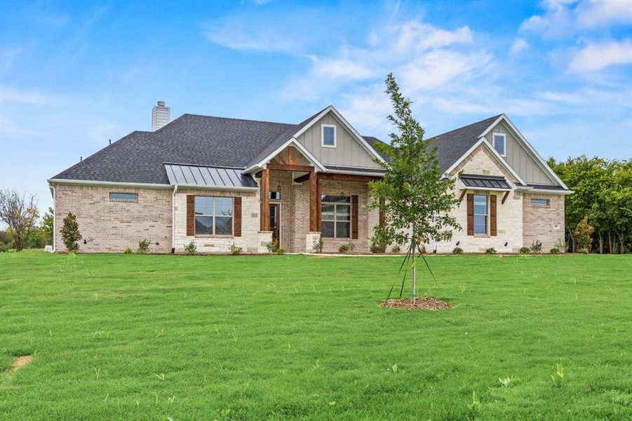 View of front of house featuring a standing seam roof, a metal roof, a porch, brick siding, and a front lawn View of front of house featuring a standing seam roof, a metal roof, a porch, brick siding, and a front lawn