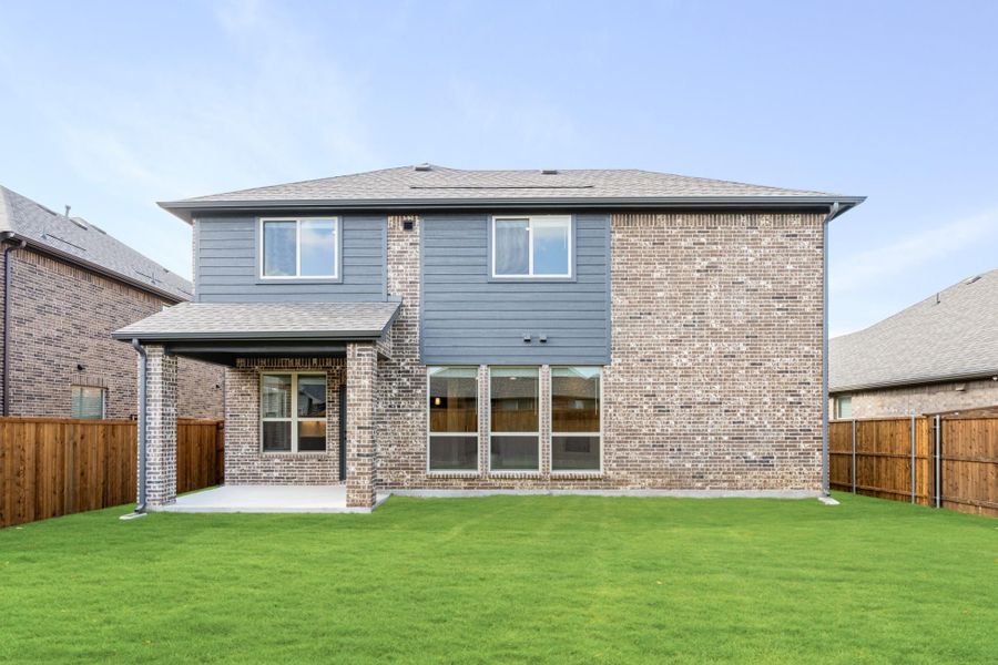 Two-story brick home rear exterior with gray siding, covered patio, and fenced backyard lawn