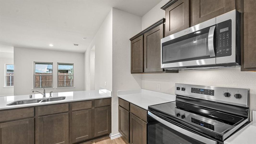 Kitchen with stainless steel appliances, light wood-style flooring, dark wood finish cabinetry, recessed lighting, and a peninsula