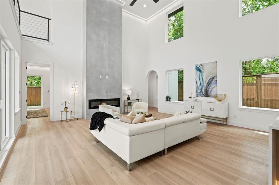 Living room with a towering ceiling, healthy amount of natural light, a ceiling fan, light wood-type flooring, and a tiled fireplace