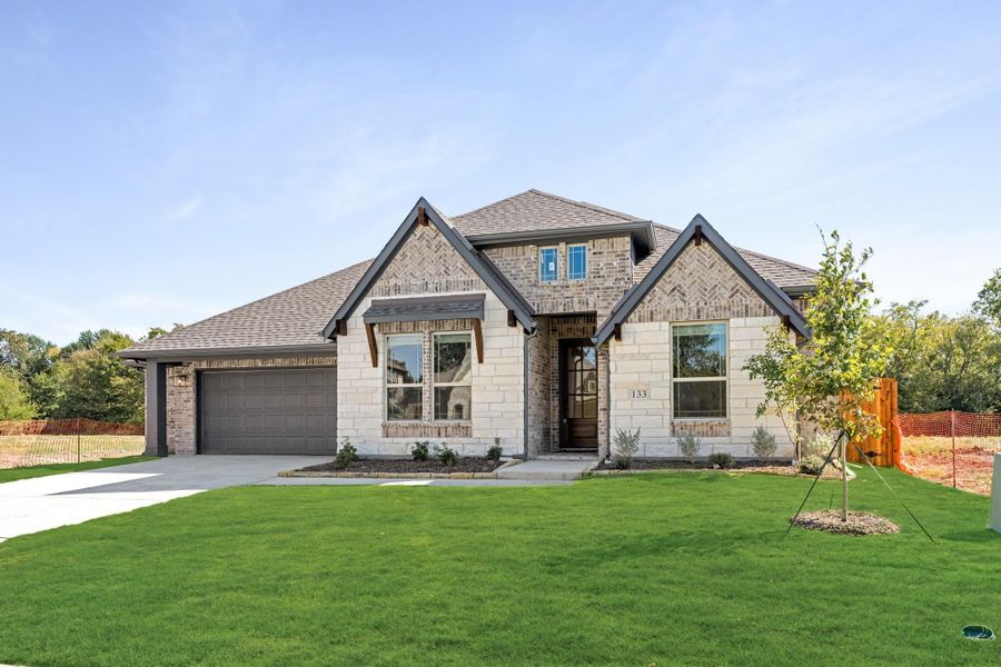 Two-story home with brick and stone exterior, two-car garage, and green front lawn Two-story home with brick and stone exterior, two-car garage, and green front lawn