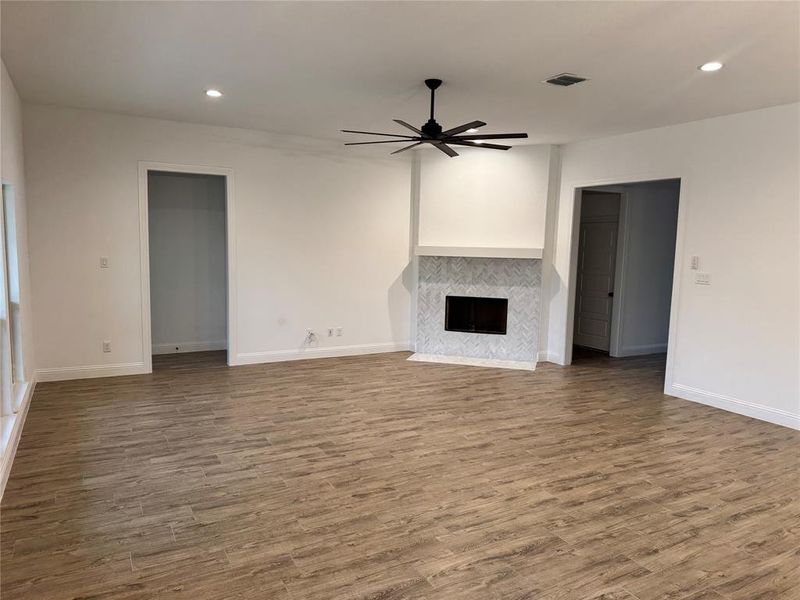 Unfurnished living room with a tiled fireplace, wood-type flooring, and ceiling fan