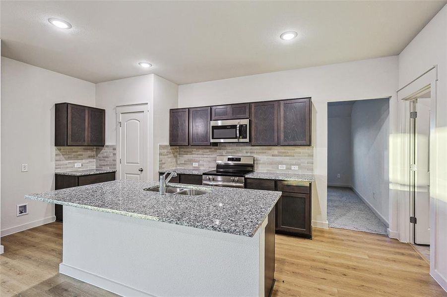 Kitchen with dark brown cabinetry, sink, tasteful backsplash, stainless steel appliances, and light wood-type flooring