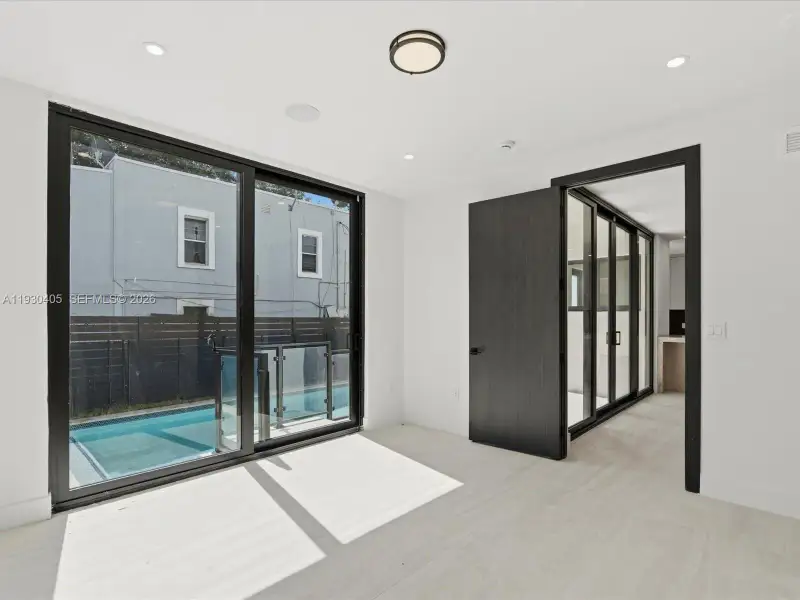 Floor-to-ceiling black-framed sliding glass doors, recessed lighting, wood-finish flooring, and solid-core dark wood interior doors Floor-to-ceiling black-framed sliding glass doors, recessed lighting, wood-finish flooring, and solid-core dark wood interior doors