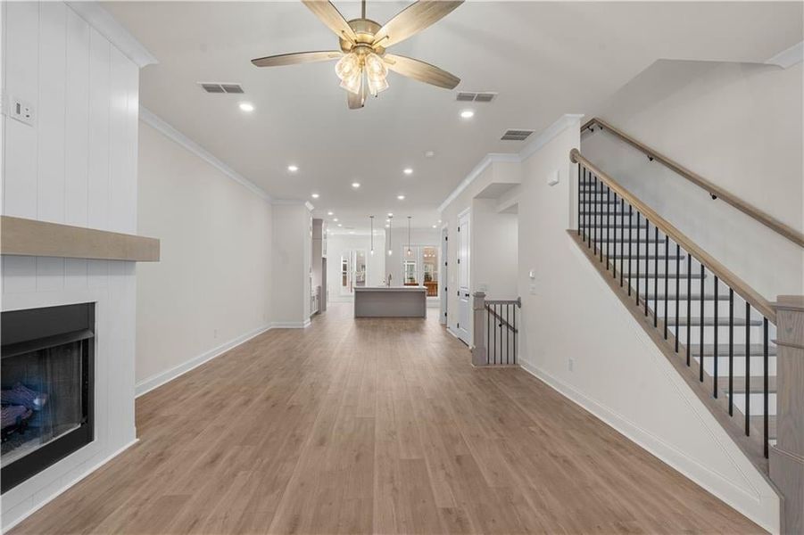 Unfurnished living room featuring a large fireplace, light wood finished floors, recessed lighting, crown molding, and ceiling fan