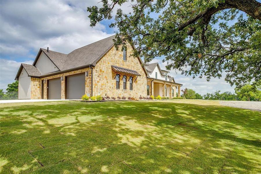 View of front of property featuring a garage, a front lawn, stone siding, and a shingled roof View of front of property featuring a garage, a front lawn, stone siding, and a shingled roof