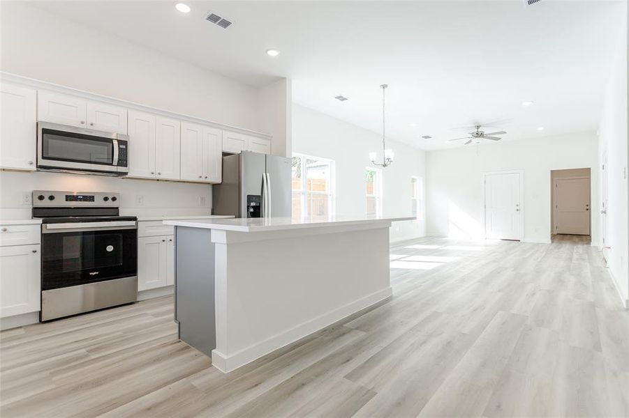 Kitchen featuring stainless steel appliances, light hardwood / wood-style floors, white cabinetry, decorative light fixtures, and a center island