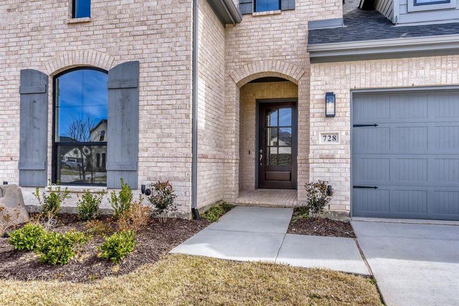 View of exterior entry featuring brick siding, a garage, stone siding, and roof with shingles