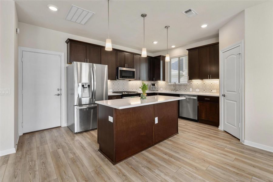 Kitchen featuring dark brown cabinets, appliances with stainless steel finishes, decorative light fixtures, a center island, and recessed lighting