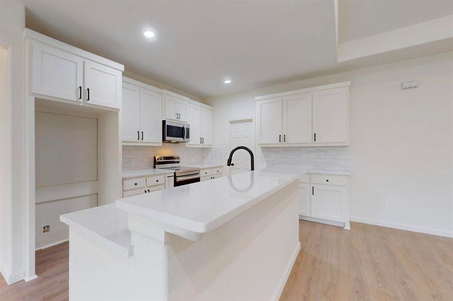 Kitchen with light wood finished floors, white cabinets, appliances with stainless steel finishes, and a kitchen island with sink