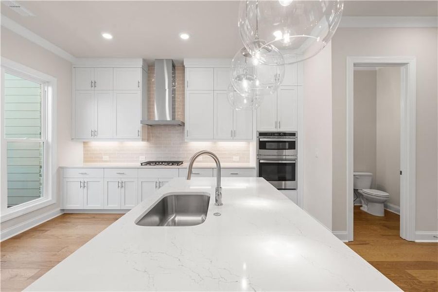 Kitchen featuring light wood finished floors, white cabinets, backsplash, wall chimney range hood, and light stone countertops
