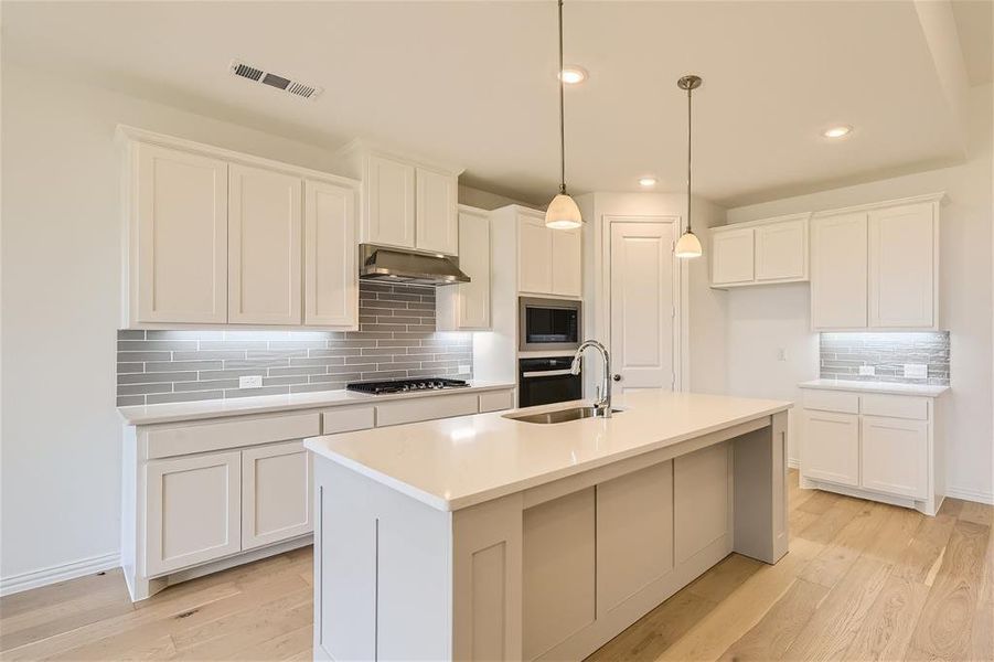 Kitchen with a center island with sink, light hardwood / wood-style flooring, white cabinets, wall chimney exhaust hood, and tasteful backsplash