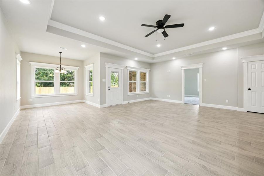 Unfurnished living room featuring a raised ceiling, crown molding, recessed lighting, a ceiling fan, and a chandelier Unfurnished living room featuring a raised ceiling, crown molding, recessed lighting, a ceiling fan, and a chandelier