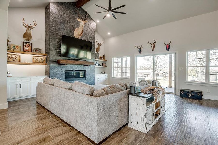 Living room with beam ceiling, high vaulted ceiling, a fireplace, and light hardwood / wood-style flooring