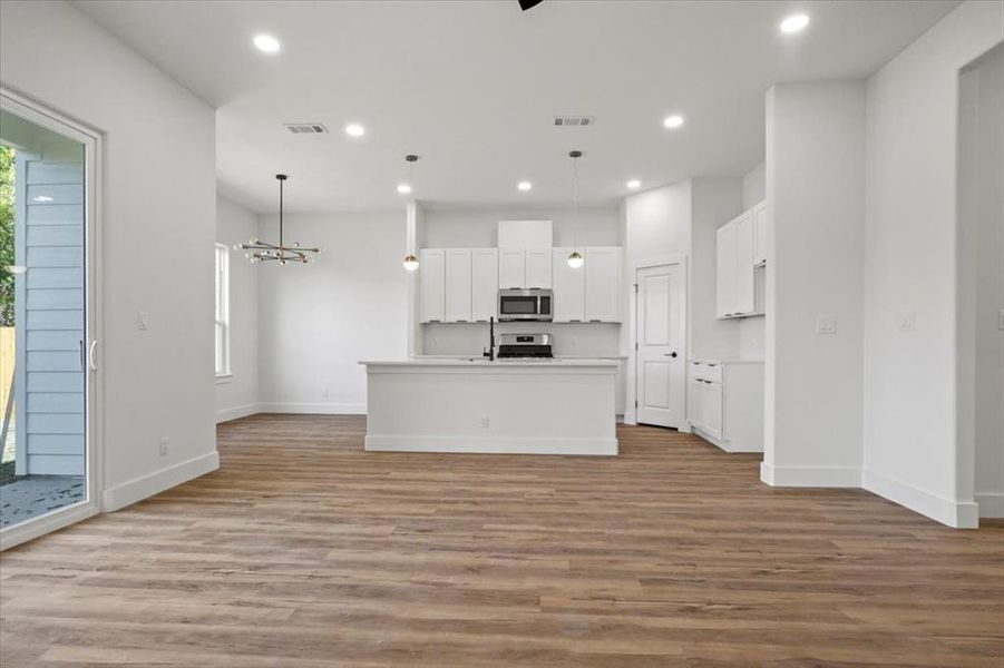 Kitchen with white cabinetry, light wood-style floors, light countertops, hanging light fixtures, and open floor plan