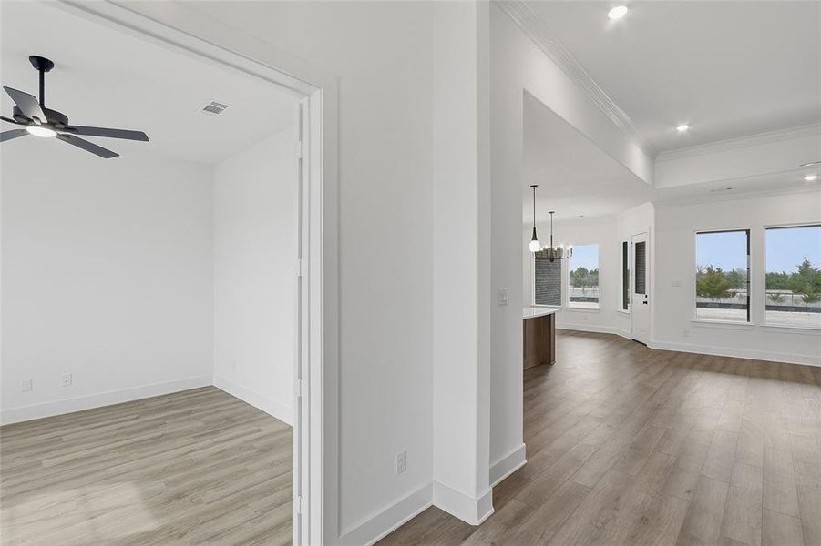 Hall with light wood-type flooring, ornamental molding, and a chandelier