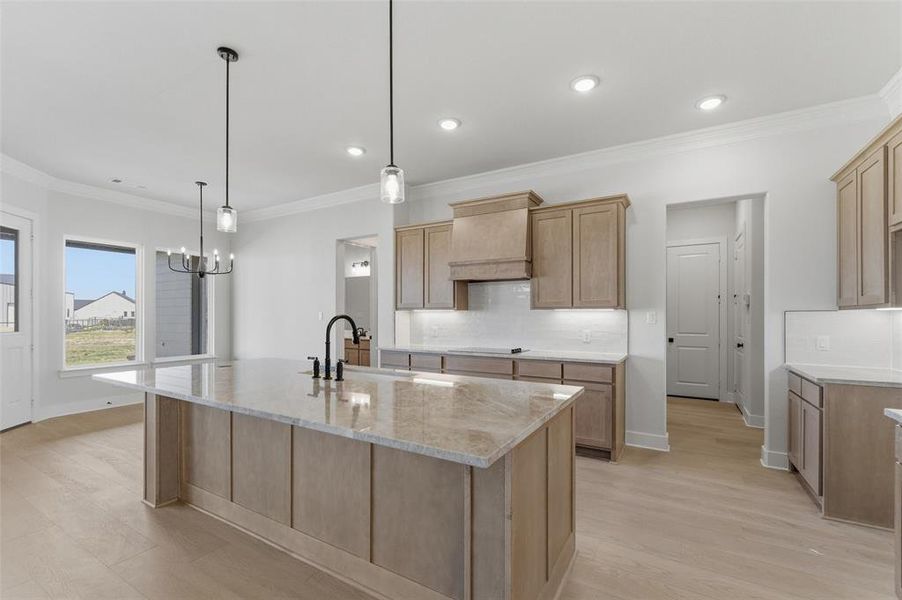 Kitchen with light stone counters, an island with sink, backsplash, crown molding, and light wood finished floors Kitchen with light stone counters, an island with sink, backsplash, crown molding, and light wood finished floors