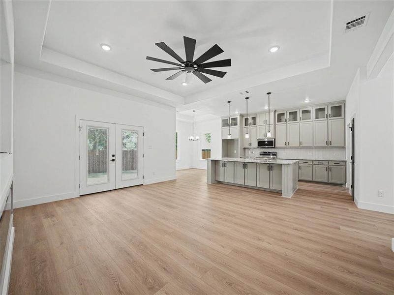 Open-concept living space featuring light wood-finish flooring, a tray ceiling with a contemporary ceiling fan, and recessed lighting Open-concept living space featuring light wood-finish flooring, a tray ceiling with a contemporary ceiling fan, and recessed lighting