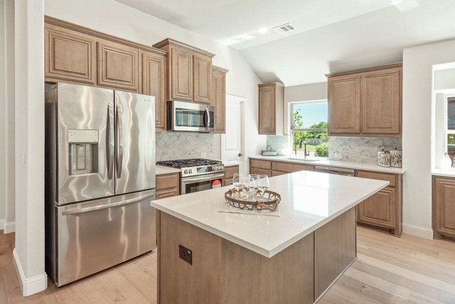 Kitchen with tan wood cabinets, center island, white countertops, and stainless steel appliances on light hardwood floors