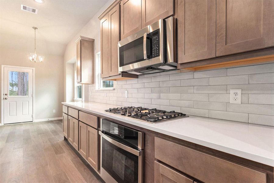 This kitchen features modern appliances, including a built-in microwave and gas cooktop. It has sleek cabinetry, a tiled backsplash, and ample counter space. Natural light enters through the window, complementing the light wood flooring and creating an inviting atmosphere.