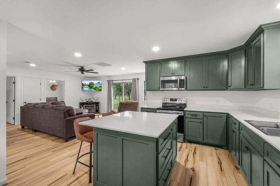 Open-concept kitchen featuring sage green cabinetry, a central island with countertop seating, and light wood-finish flooring
