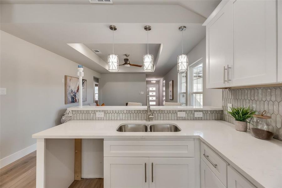 Kitchen featuring white cabinets, sink, hanging light fixtures, backsplash, and light hardwood / wood-style floors